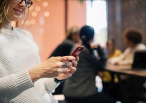 Blonde businesswoman standing in office while sending customers a message through a business text messaging app on her phone