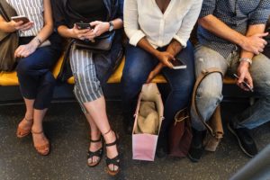 Four people on a subway holding their phones, checking appointment reminders sent through business texting