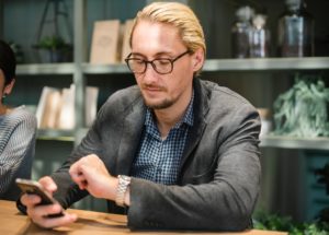 Blonde man checking his watch after reading SMS appointment reminder on his phone