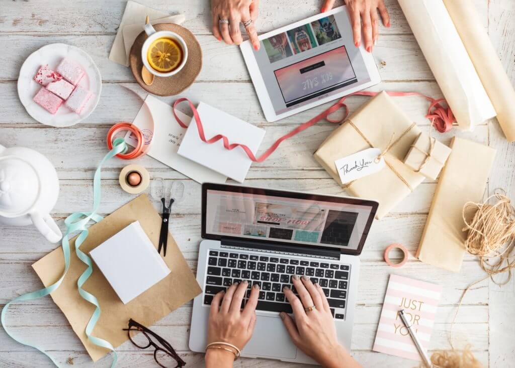 Flat lay of work table covered in ribbons, scissors, and a laptop and tablet where team members are creating an SMS campaign