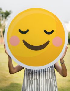 Woman holding up giant smiley face emoji poster in front of her face