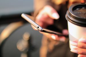 Small business team member with coffee in one hand checking customer messages on her business SMS app