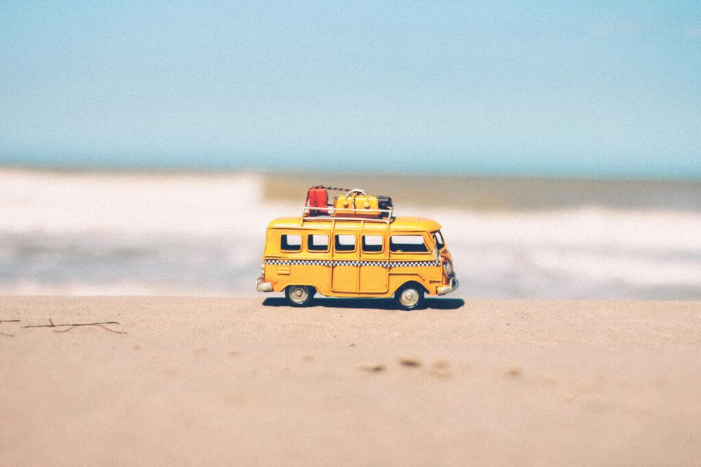 Yellow toy bus with luggage on top of the white sand of a beach
