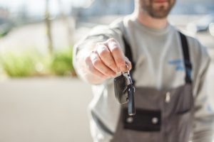 Service team member wearing coveralls holding out keys for test drive scheduled through automotive business text messaging