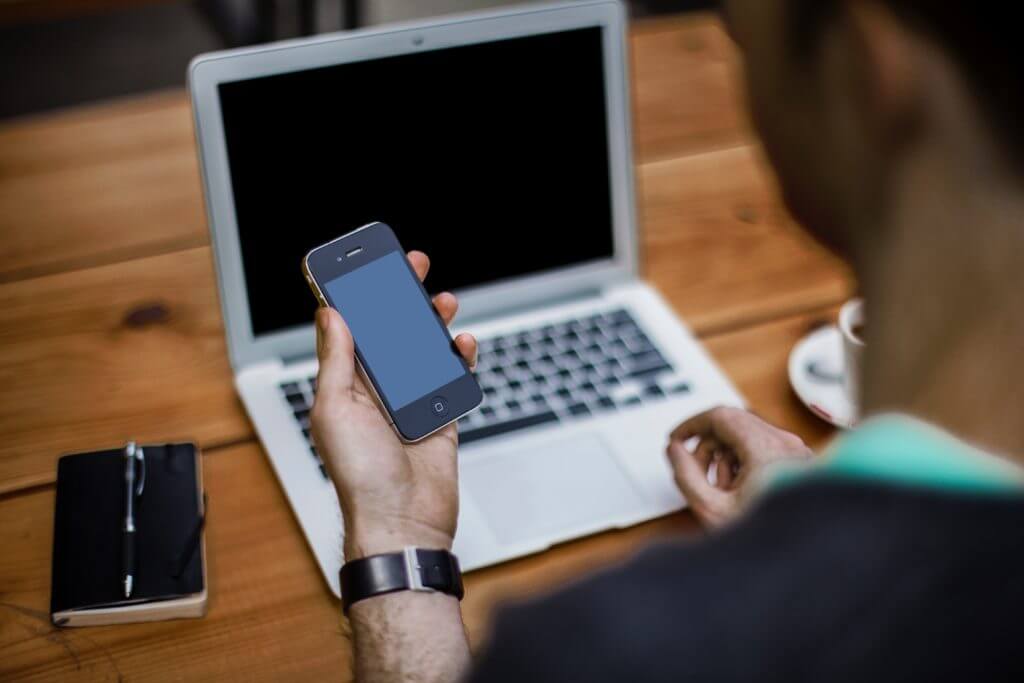 Man at computer looking at phone.