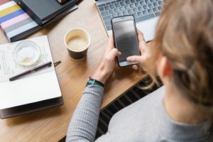 Person at desk with cell phone and laptop.