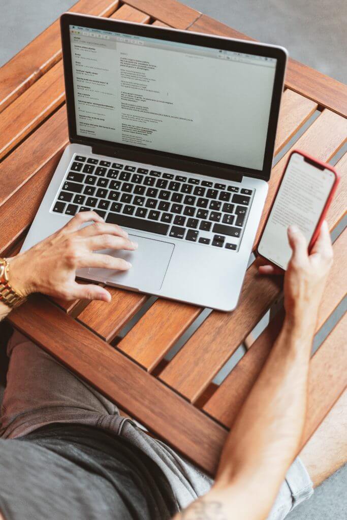 Person working on computer and holding phone.