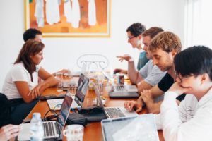 Team of seven sitting at large table working on laptops to answer incoming customer messages