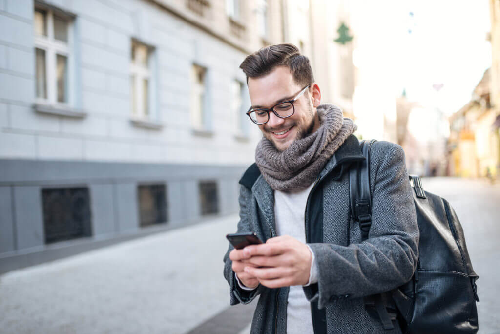 Customer outside in city street smiling while replying to a text