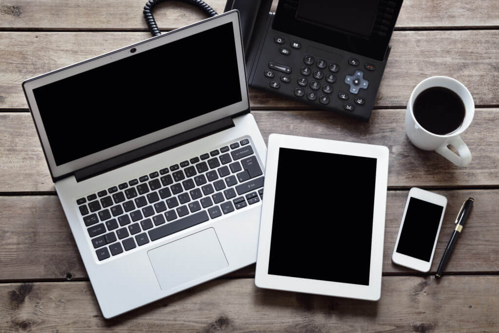 Laptop, desk phone, tablet, smartphone on desk.