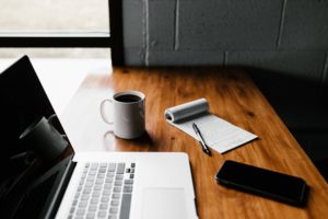 Desk with laptop, phone, coffee cup, and open notebook for brainstorming SMS template ideas