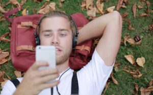 Student lying on grass with phone in hand reading college SMS message
