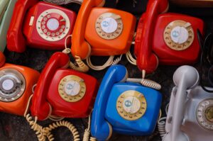 Seven blue and red old-fashioned rotary landline phones in two rows