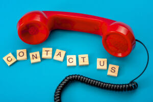 Red phone over blue background with Scrabble letters spelling 'contact us'; shows traditional method compared to business SMS 