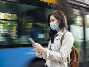 Masked woman receiving a business SMS message while waiting for bus
