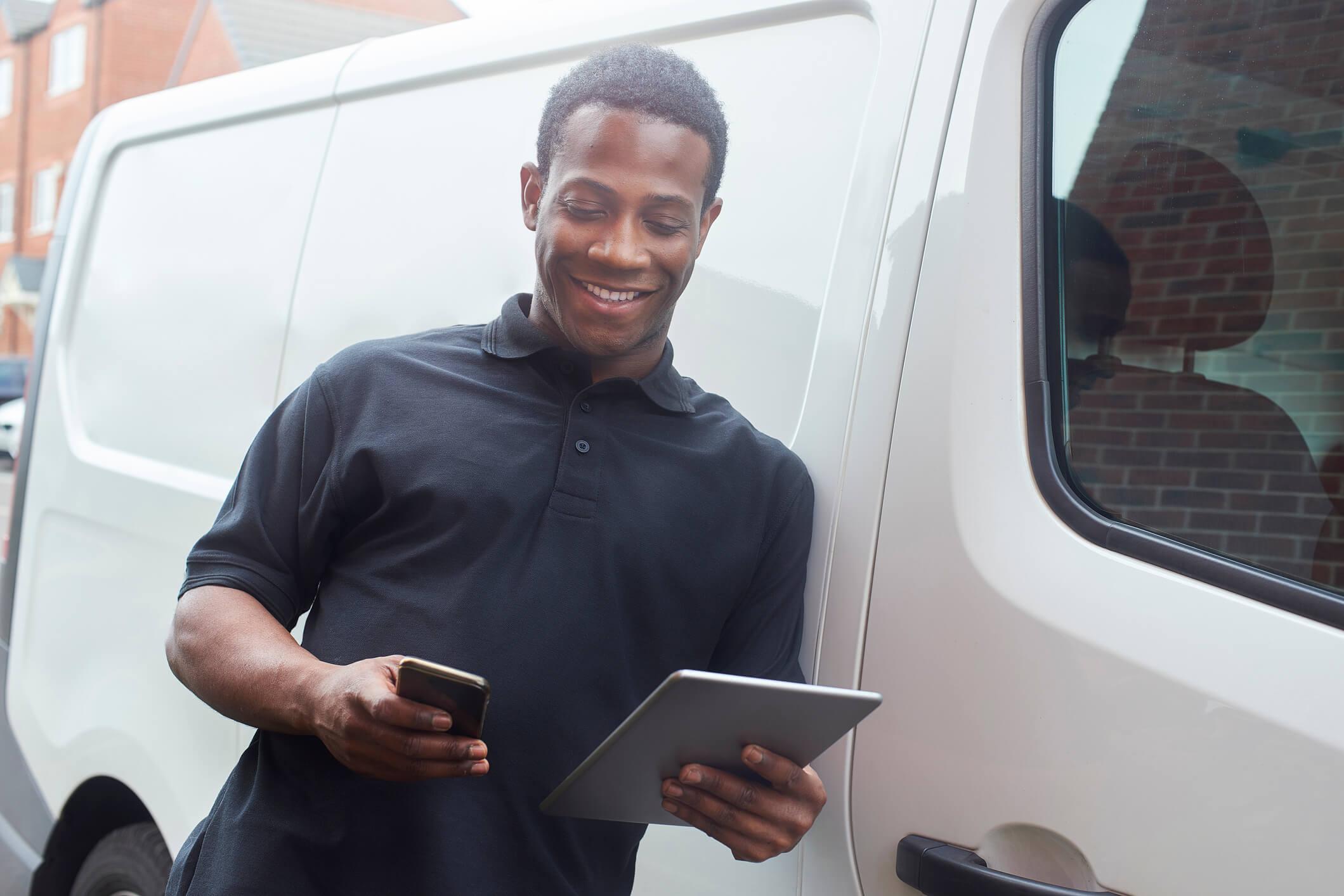 Tradesman leaning against van to text