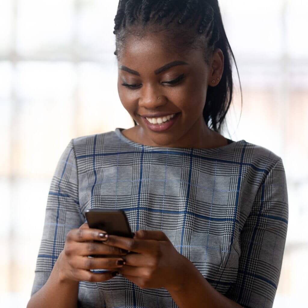 Saleswoman smiling as she uses conversational customer engagement software on her mobile phone