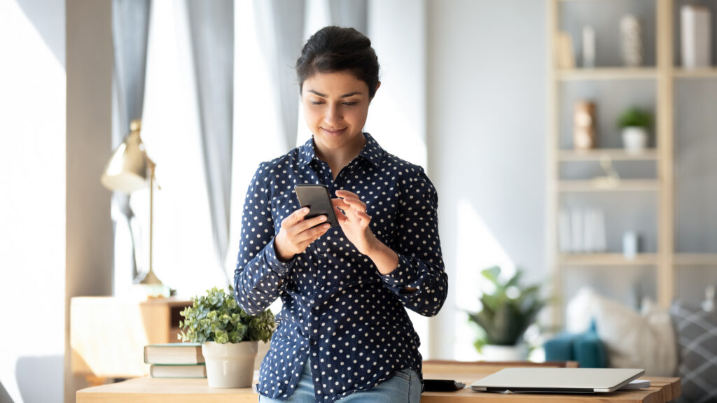 Woman leaning against desk and texting using Conversational Customer Engagement.