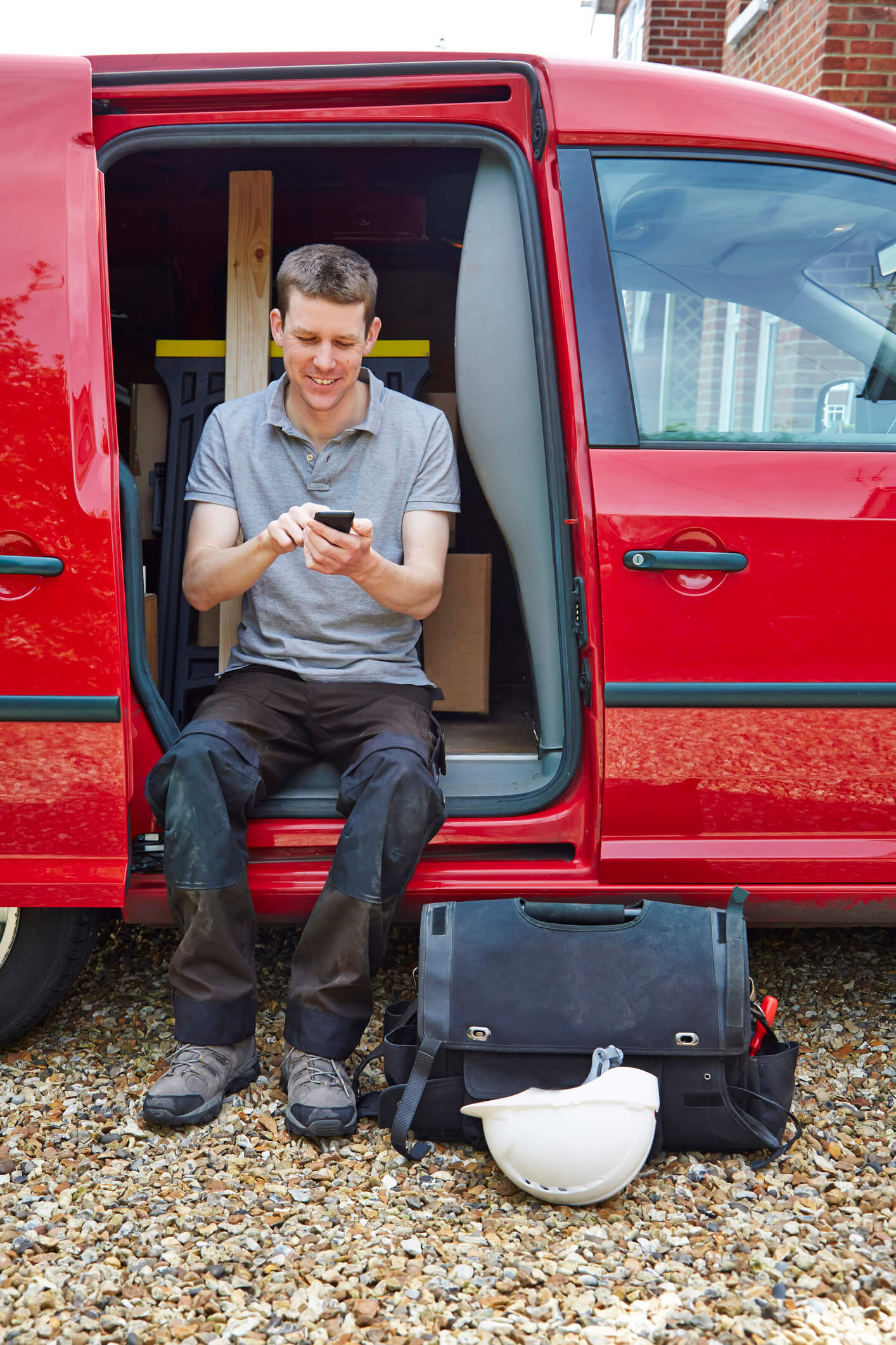 Man sitting in van with utility case texting