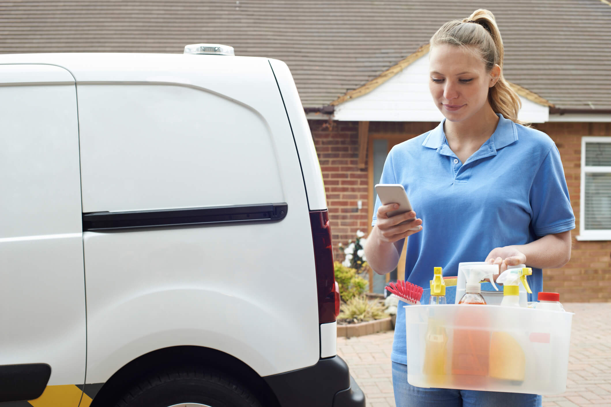 Woman in polo shirt with cleaning basket texting