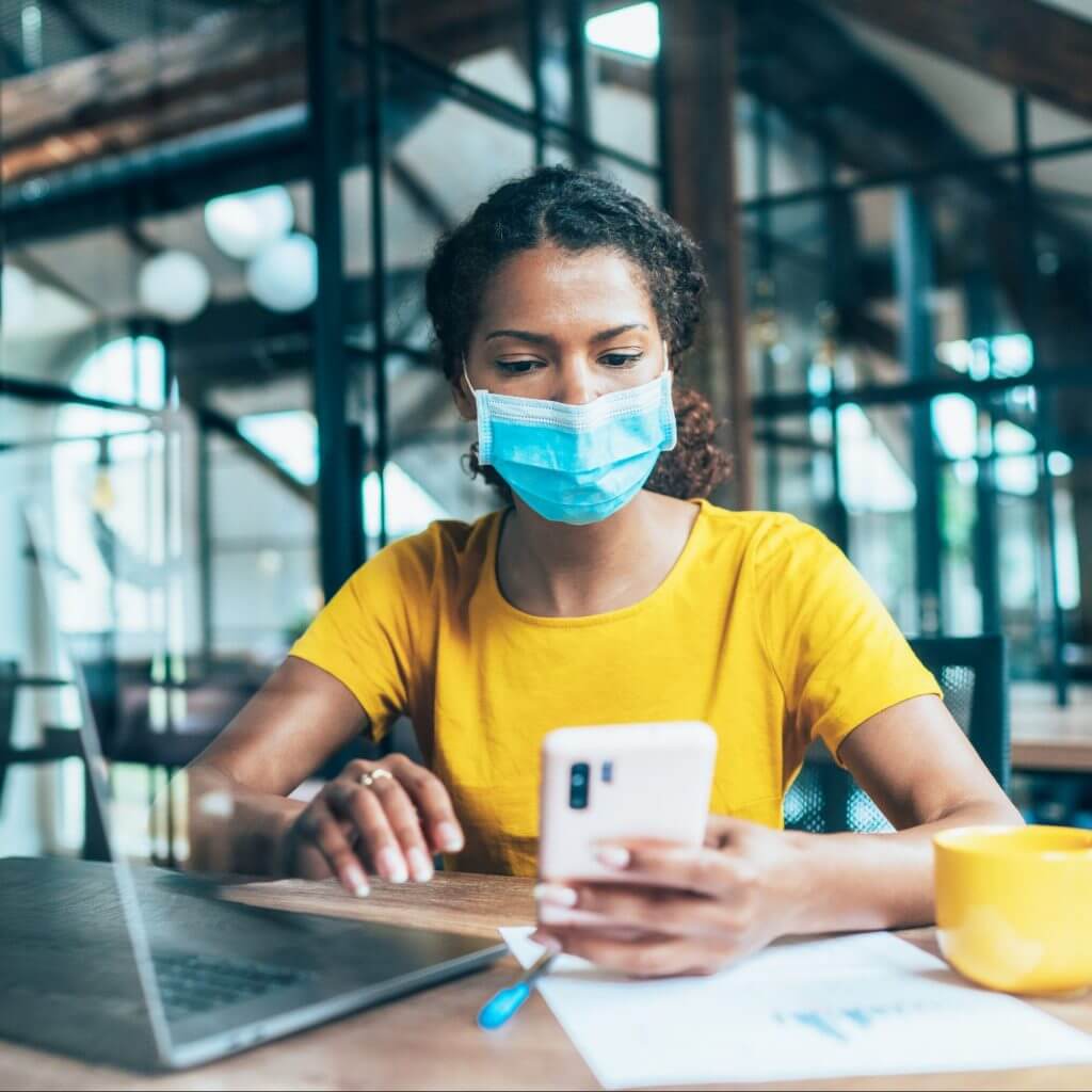Business woman in mask texting, illustrating the benefits of texting in business during the pandemic