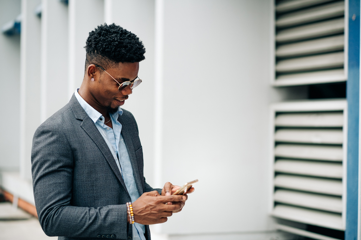 Businessman in sunglasses smiling down at phone while using business texting