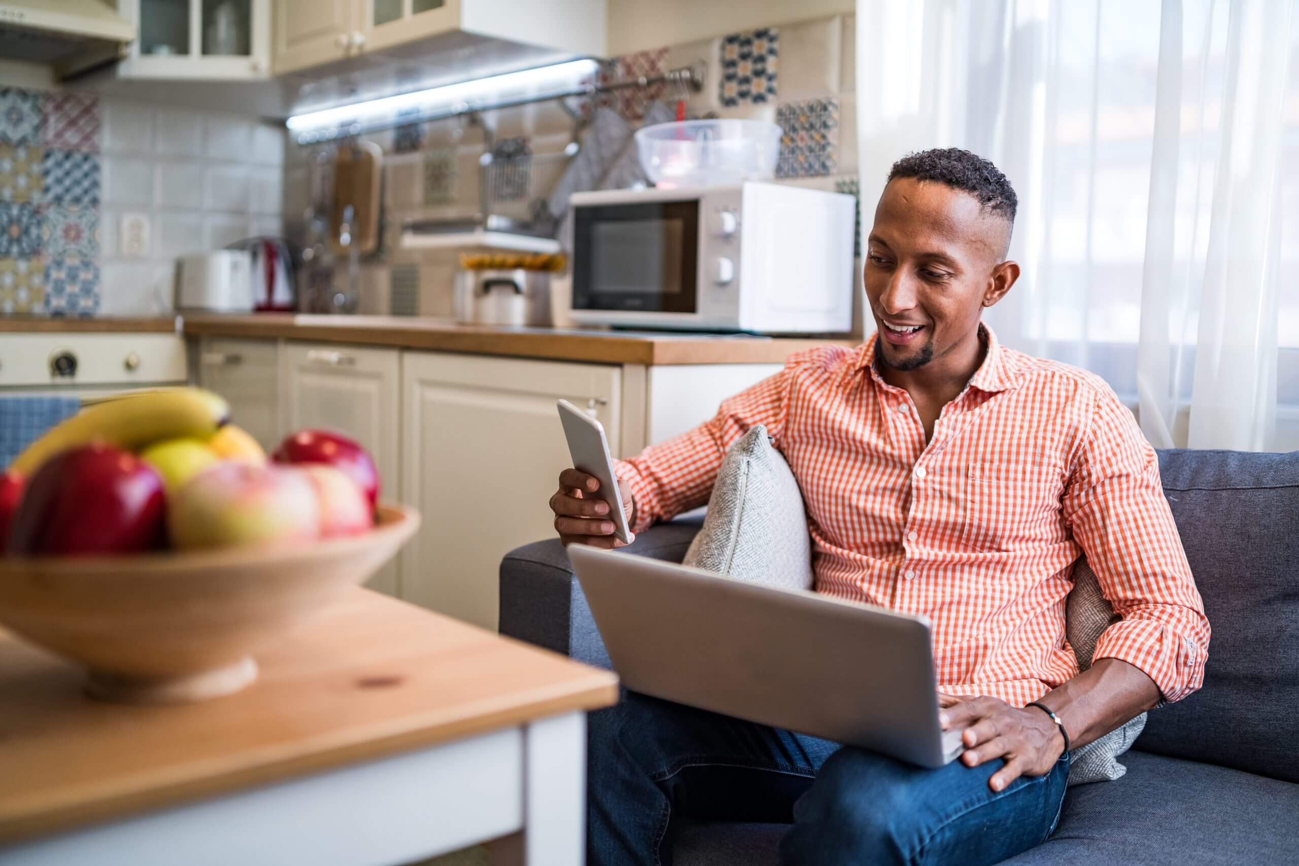 Man shopping using phone and computer on couch using ecommerce sms resources