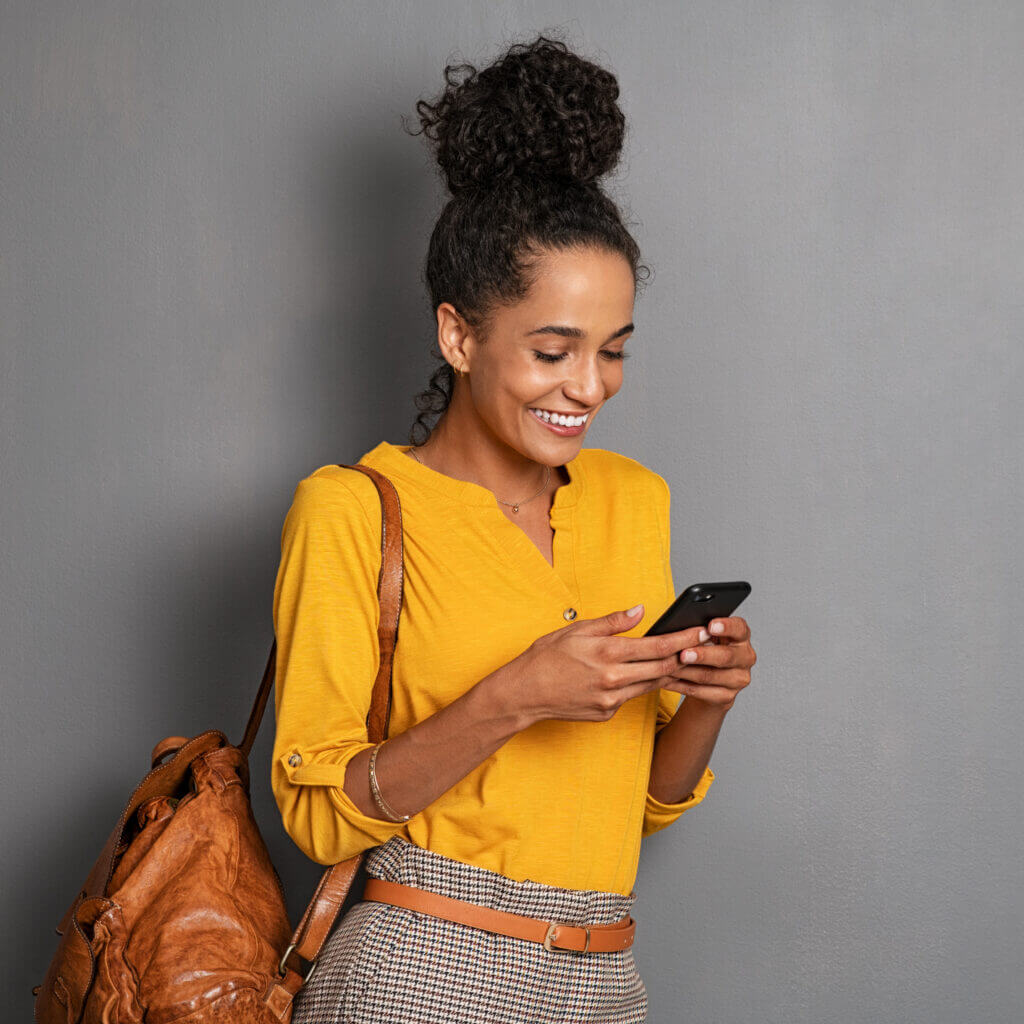 Woman in yellow learning against a wall and texting using conversational support