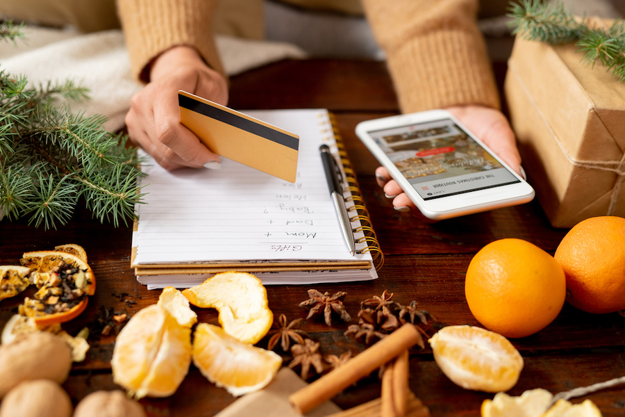 Woman's hands holding a smartphone and credit card surrounded by holiday decorations