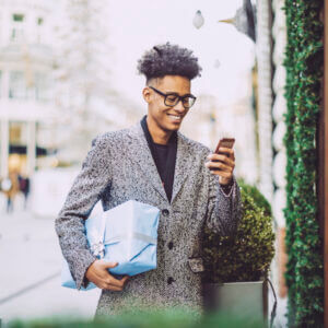 A holiday shopper holding a gift and texting