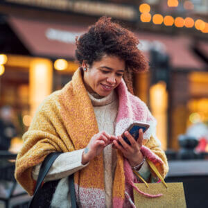 Woman wearing winter clothes texting outside of a store