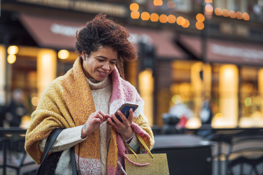 Woman wearing winter clothes texting outside of a store