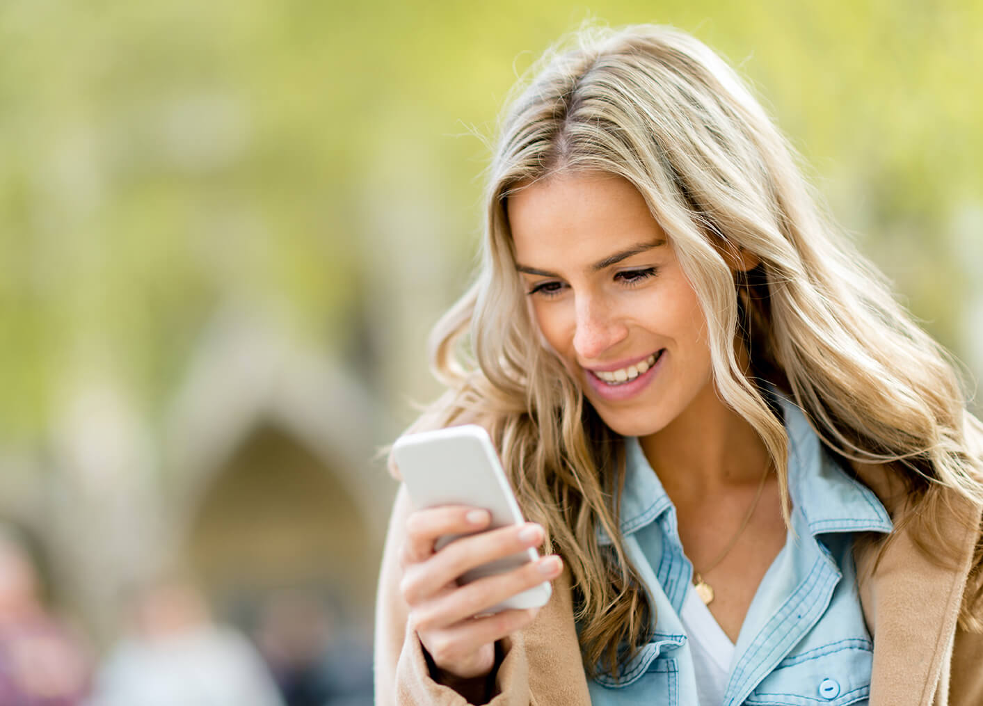 Blonde client standing outdoors and smiling at SMS reminder for upcoming meeting