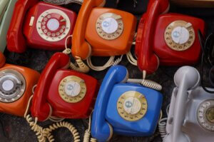 Seven blue and red old-fashioned rotary landline phones in two rows